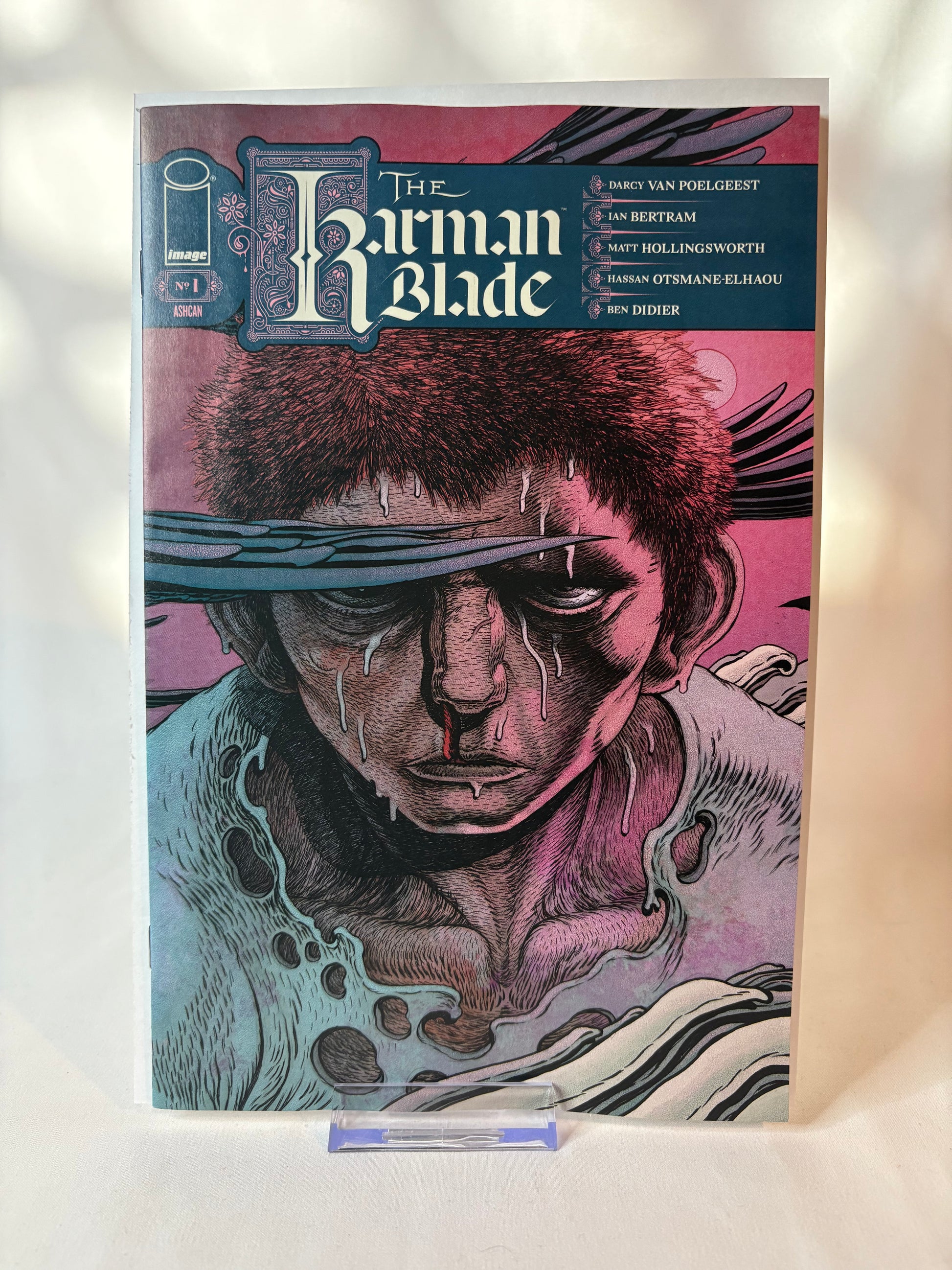 The Harman Blade #1 comic book cover displayed upright on a small clear stand against a light fabric background.
